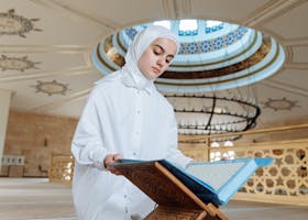 A young woman reading the Quran in a beautifully decorated mosque, symbolizing faith and spirituality.